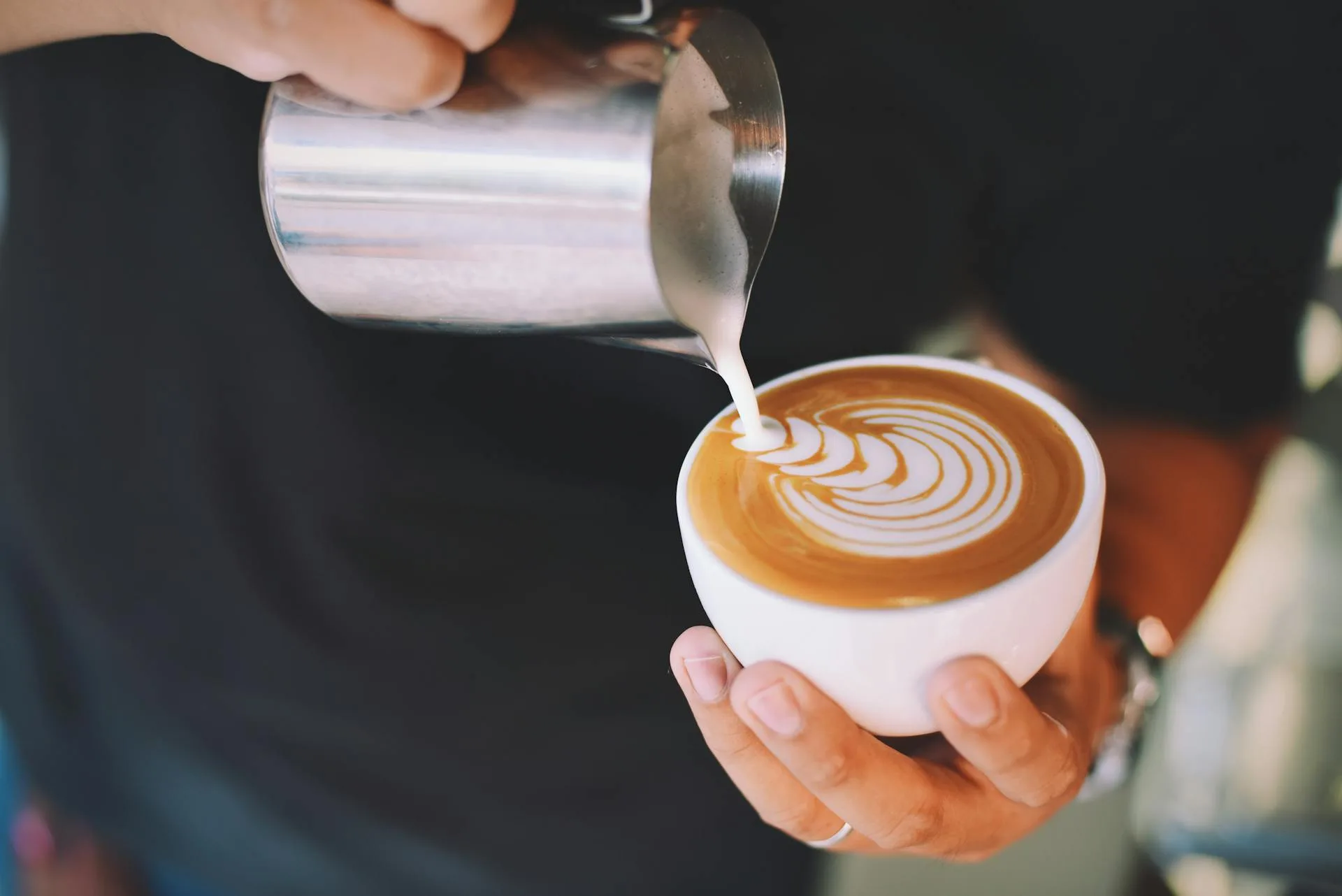 Barista pouring steamed milk to create latte art in a cappuccino cup