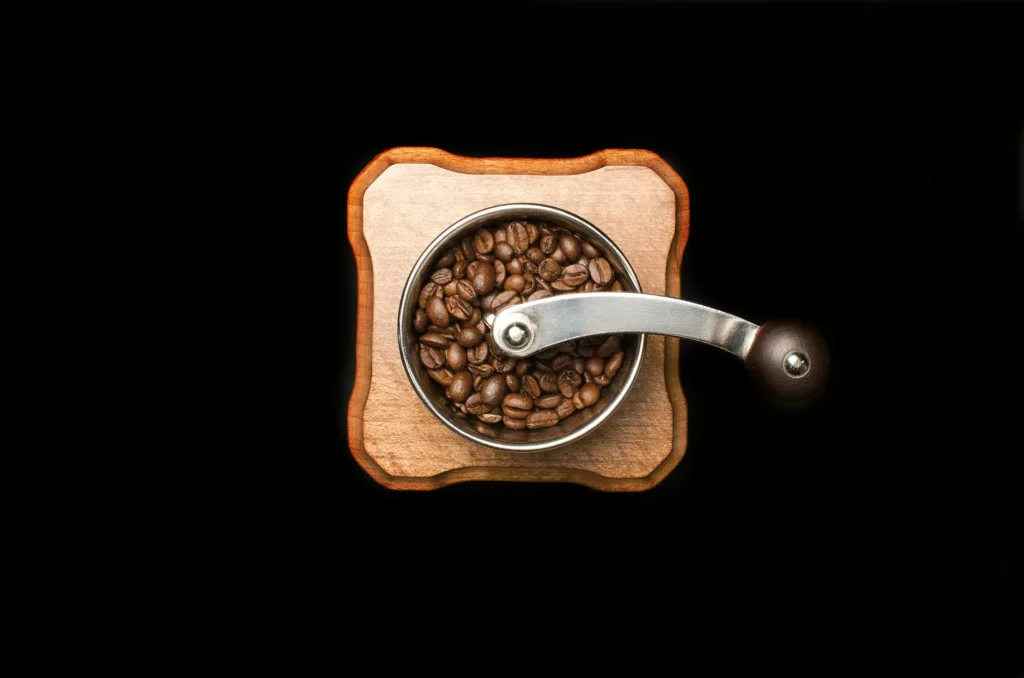 Coffee beans beside a burr grinder showing freshly ground coffee