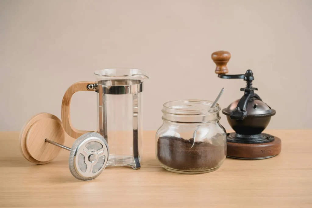 Coffee grinder with beans next to a French press on a counter