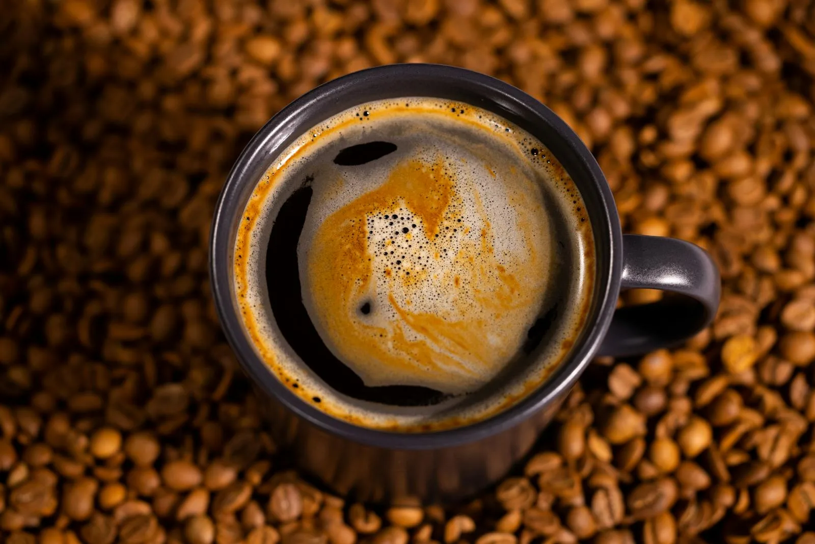 Rich espresso in a dark mug surrounded by dark roasted coffee beans