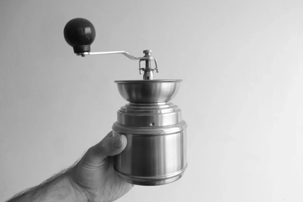 Hand coffee grinder with freshly ground coffee beans on a wooden surface