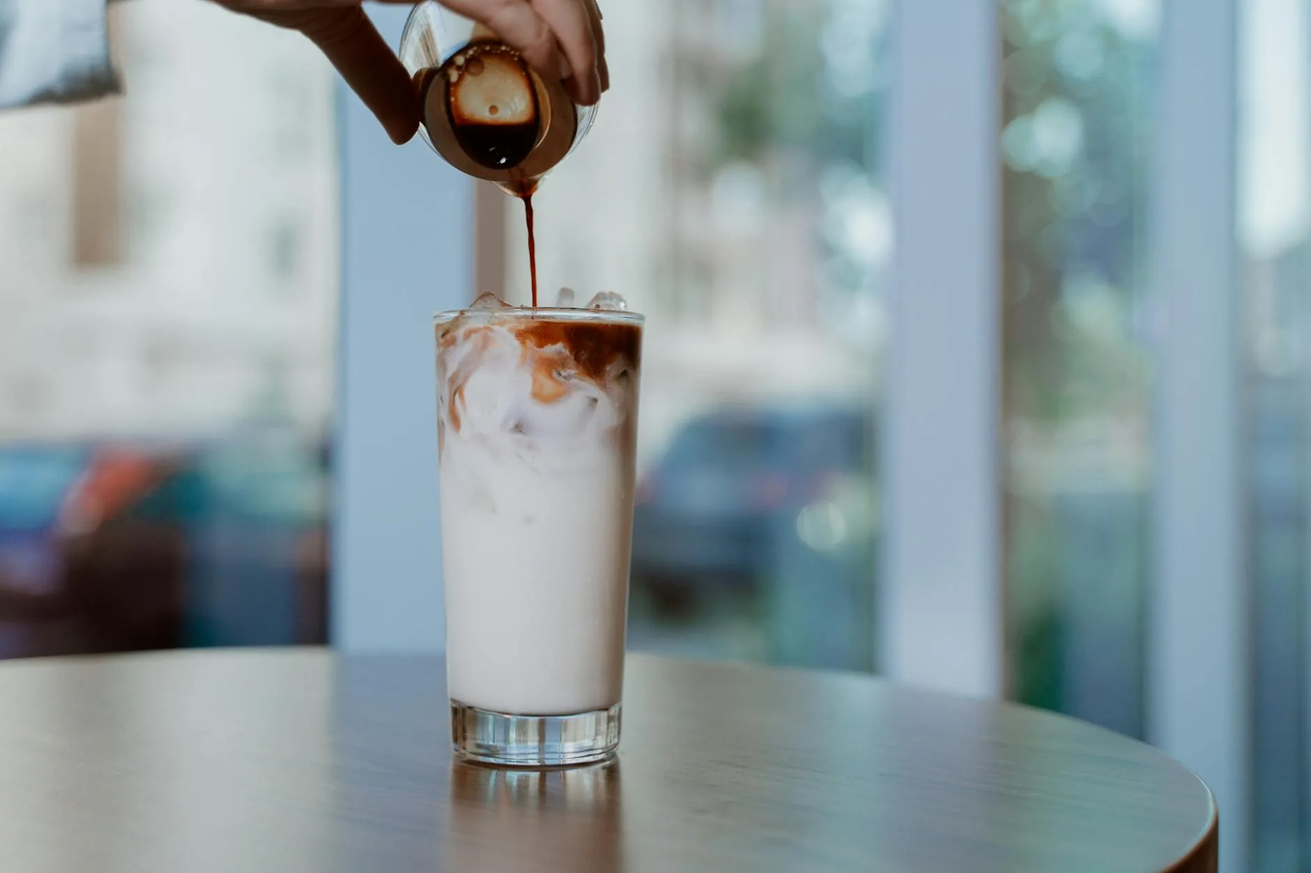 Milk being poured into a glass of iced coffee