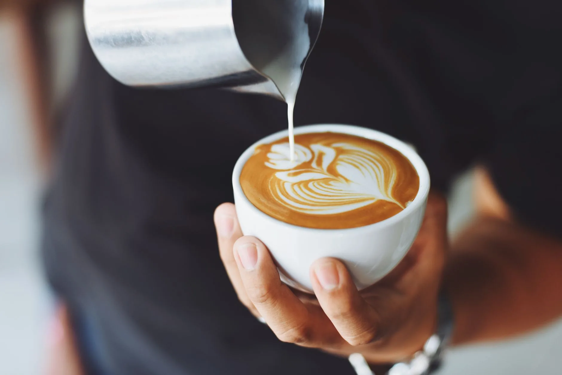 Home barista pouring latte art into a coffee cup